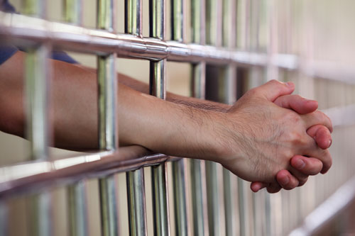 mans hands sticking out of jail cell bars | Boulder crime lawyers